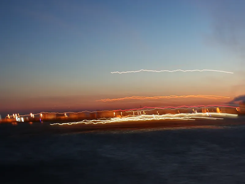 Bateau en mouvement immortalisé avec un temps d'obturation long. Le ciel est dégradé de rose et de bleu tandis que le bateau ne laisse derrière son passage que des trainées lumineuses abstraites.