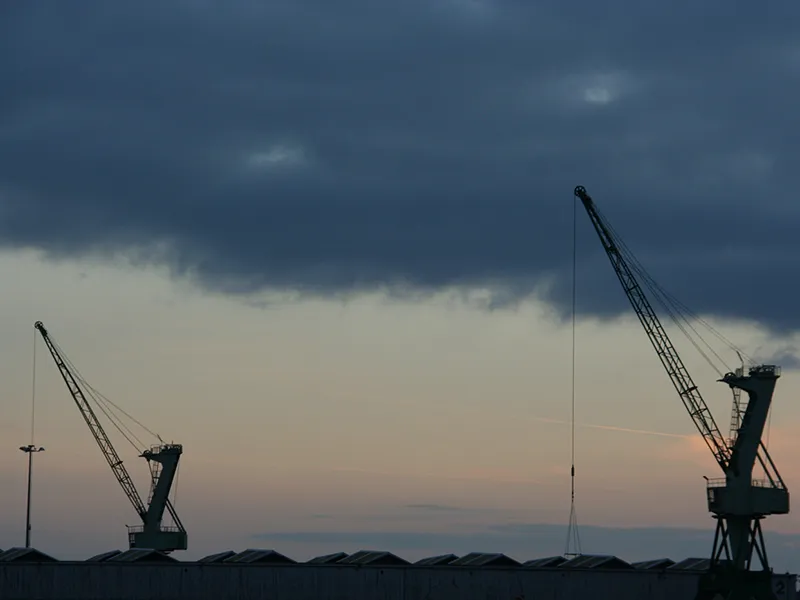 De grandes grues métalliques créent de la dentelle noire sur l'arrière plan nébuleux du coucher de soleil et des nuages.