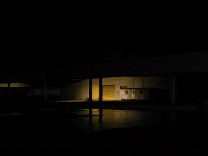 Une lumière jaune éclaire l'entrée d'un entrepôt, tout le reste est obscurité.